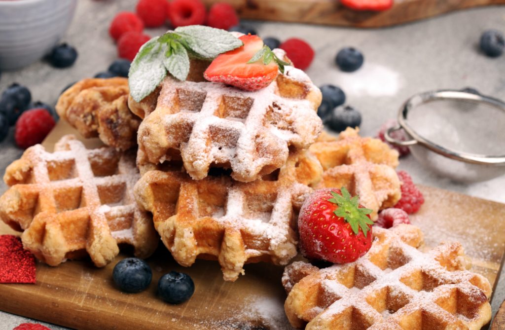Traditional belgian waffles with fresh blueberries, sugar and raspberries on wood
